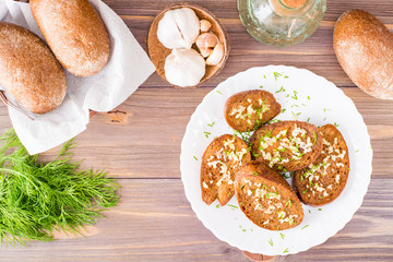 Fresh rye garlic croutons with dill on a plate and buns in a basket on a wooden table. Top view.