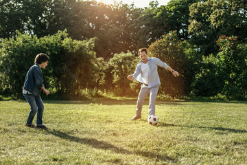 Best team. Happy concentrated smiling father and son spending time together and playing football in nature while the father is going to hit the ball