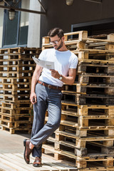 Fototapeta premium Fashionable confident businessman smoking cigar and reading report by wooden palettes