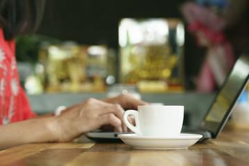 close up of cup coffee beside freelanceer woman,she is working by using the laptop computer.