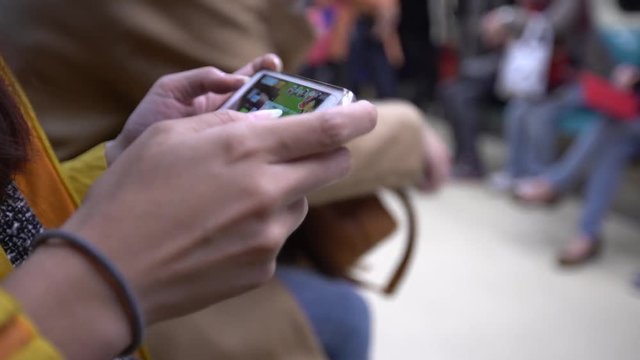 4K Asian young woman sit down in a metro plays game with phone at train station Taiwan. Passenger using technology smartphone in MRT subway for travel in city, lifestyle and transportation concept-Dan