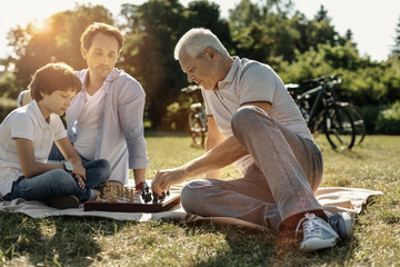 I love chess. Concentrated grey-haired grandpa sitting on the grass and playing chess with his...