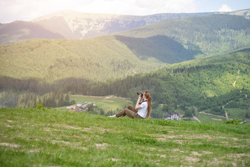 Girl with camera sits on a hill and mountain photographs. Summer day