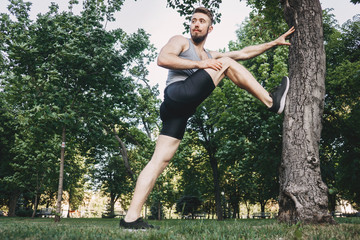 Sportsman doing stretching exercise before run. Muscular runner preparing for morning workout in the park. Street fitness, sport, exercising, people and healthy lifestyle concept.