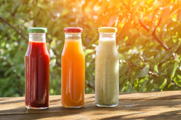 Three bottles of juice in the garden on a background of greenery. Summer, sunlight