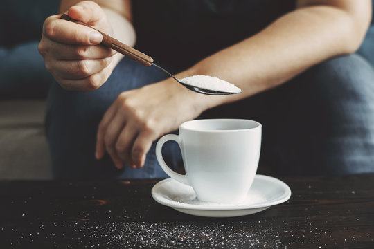 Sugar addiction, unhealthy lifestyle, weight gain, dietary, healthcare and medical concept. Cropped portrait of woman pouring sugar into coffee cup