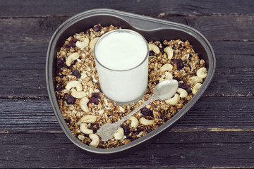 Glass of yogurt and granola with cashews on a baking sheet. Black wooden table