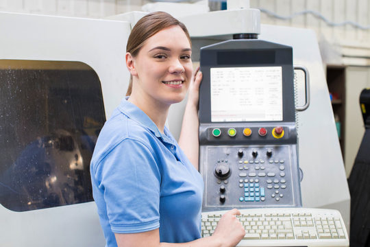 Portrait Of Female Apprentice Engineer Operating CNC Machine In Factory