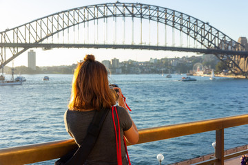 Fototapeta premium Female tourist with backpack bag taking photos of Sydney Harbour Bridge during summer vacation trip.