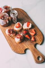 top view of cutting board with fruit jam in jars and sandwiches with cream cheese and jam on marble table