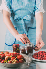 partial view of woman doing jam from strawberries and raspberries at kitchen