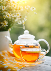 Cup with hot tea with mint and a thyme on a wooden table in a summer garden.