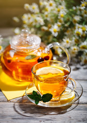 Cup with hot tea with mint and a thyme on a wooden table in a summer garden.
