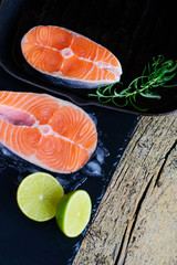 Two salmon steaks are ready to cook on a grill, along with lime on a wooden background. Top view. Healthy food
