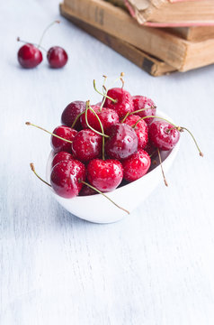 Fresh red cherry in a white bowl on wooden table and a books on background