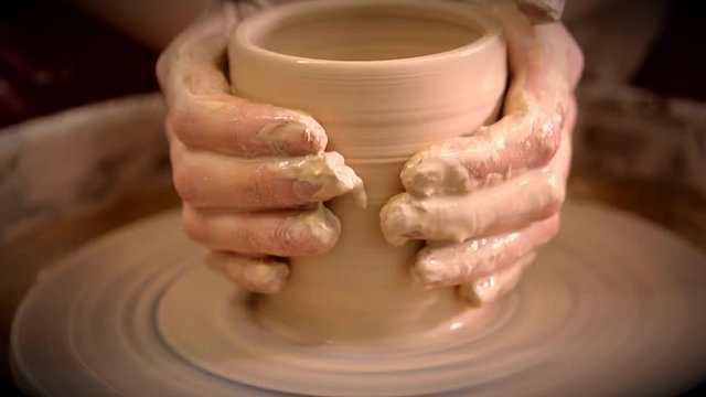 Creating vase of white clay close-up. The sculptor in workshop makes jug out of clay closeup. Twisted potter's wheel. Master crock. Potter's work close-up. Man hands making clay jug. Handmade. Craft.