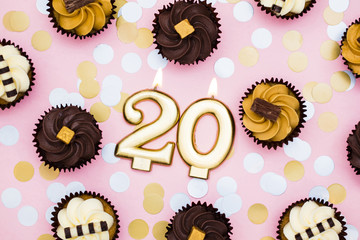 Number 20 gold candle with cupcakes against a pastel pink background