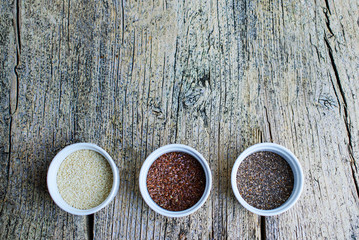 Three superfoods chia, flax and sesame seeds in white pals on a wooden background