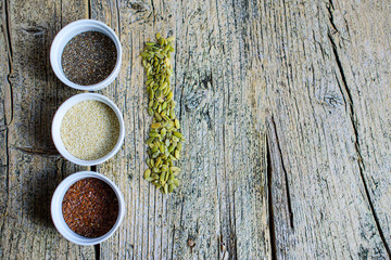 Three super foods chia, flax and sesame seeds in white pals on a wooden background, and next to the seeds of pumpkin. Top view