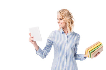 smiling attractive woman looking at tablet and holding books isolated on white