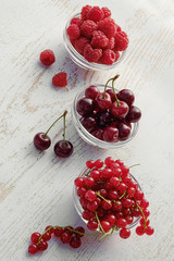 Fresh raspberries, red currants and cherries in glass bowls. vertical