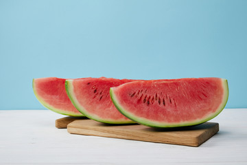 close up view of arranged watermelon slices on cutting board on white surface on blue backdrop