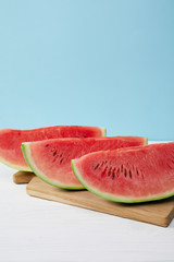 close up view of arranged watermelon slices on cutting board on white surface on blue backdrop
