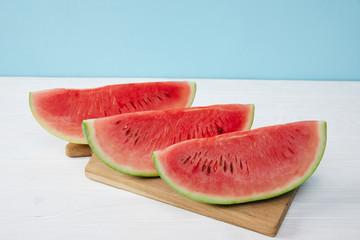 close up view of arranged watermelon slices on cutting board on white surface on blue backdrop