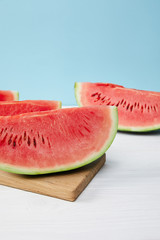 close up view of arranged watermelon slices on cutting board on white surface on blue backdrop