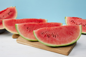 close up view of arranged watermelon slices on cutting board on white surface on blue backdrop