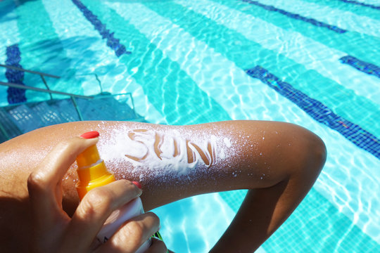 Sun text on sunscreen applied with spray on woman arm at poolside
