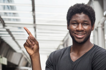 Happy African man pointing; portrait of happy smiling confident young adult african man pointing up; point raising concept; west African young adult man model