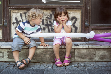 Little boy looking at girl sitting on the street in the city