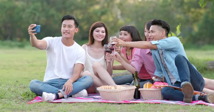 Friends taking selfie by mobile phone together in the picnic time at outdoor park