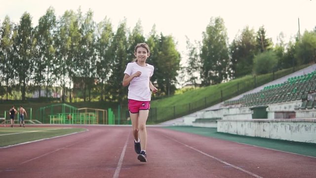 the child of 8 years is engaged in sports in stadium. the little girl is running along the path in the stadium. slow motion