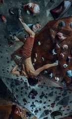 Free climber young man climbing artificial boulder indoors
