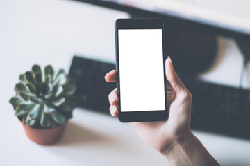 Mock up. Female hand holding a phone with white screen of working business environments.