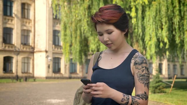 Asian beautiful young women with tattoo standing and holding phone in park near university, student texting on phone