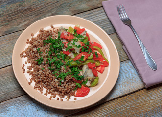 buckwheat porridge with garnish of fish blue whiting baked with vegetables, tomatoes, bell pepper and onion on a wooden table, top view close-up