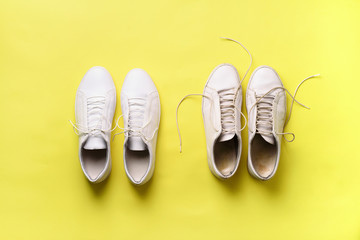 Old dirty sneakers vs new white sneakers on yellow background. Trendy footwear. Top view. Concept...