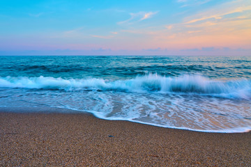 Sunset at the beach, waves with foam hitting sand.