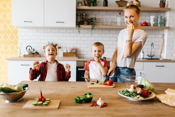 Photo of young mother with daughter and son cutting vegetables at table