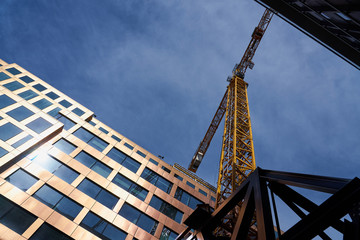 Fototapeta premium Yellow construction crane in the sunlight between houses against a blue cloudy sky.