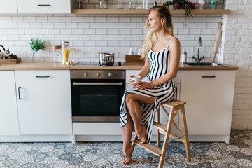 Photo of beautiful woman in long striped dress in kitchen