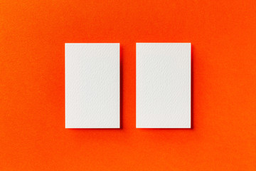Mock up of two vertical white blank business cards isolated at orange paper background.