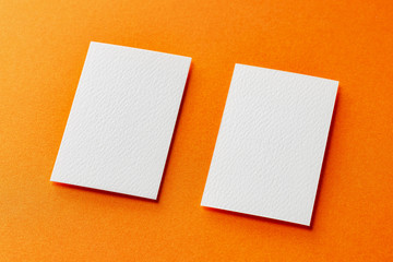 Mock up of two vertical white blank business cards isolated at orange paper background.