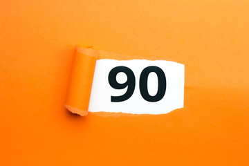 Zahl neunzig - 90 verdeckt unter aufgerissenem orangen Papier