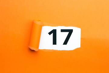Zahl siebzehn - 17 verdeckt unter aufgerissenem orangen Papier
