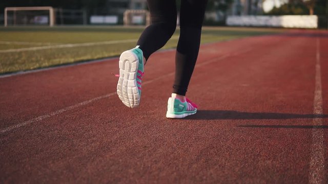 women's feet in sneakers close-up. the girl runs along the track at the stadium. the view from the back. slow motion