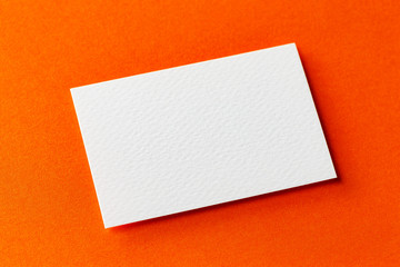 Mockup of single white business card isolated at orange textured design paper background.